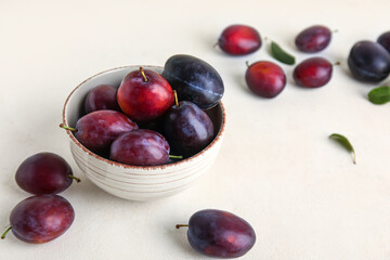 Bowl with fresh ripe plums on white background