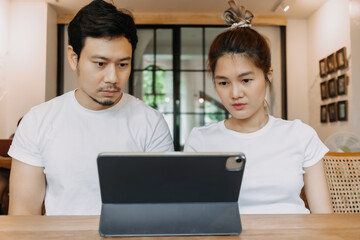Straight faces of asian man and woman working with computer tablet in cafe.