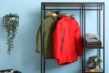 Clothes rack with puffer jackets near blue wall in hall