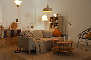 Interior of living room with sofa, table and glowing lamps in evening