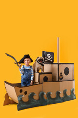 Little girl with toy sword and pug dog in cardboard pirate ship on yellow background