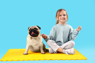 Sporty little girl with cute pug dog meditating on blue background
