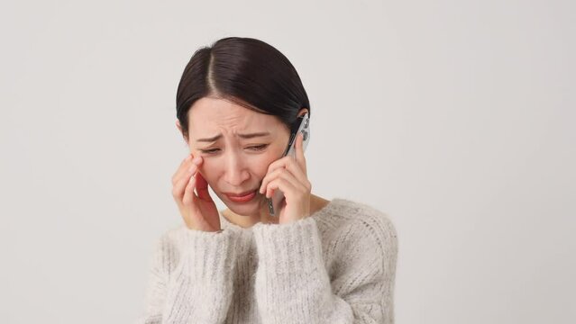 スマートフォンで通話しながら泣く女性　白背景