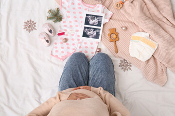 Pregnant woman with sonogram image, baby accessories and Christmas decorations on bed