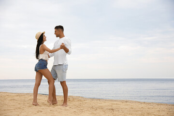 Lovely couple dancing on beach near sea. Space for text