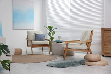 Comfortable beige armchairs, ottoman and houseplant in living room. Interior design