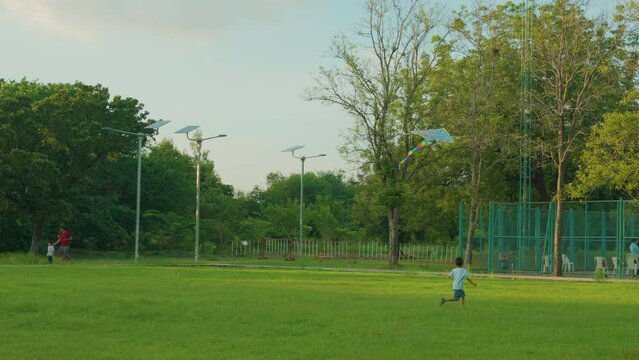 Little asian kindergarten boy running with kite in the green grass field on summer day in the city park