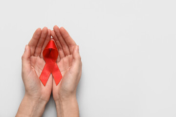 Woman with red ribbon on light background. AIDS Day concept