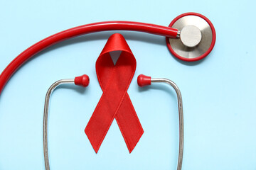 Red ribbon with stethoscope on blue background, closeup. AIDS Day concept