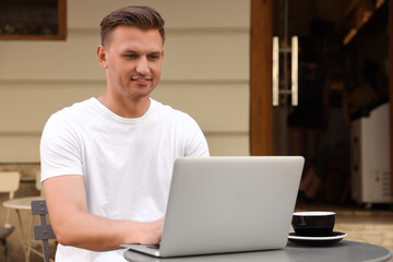 Handsome man working on laptop at table in outdoor cafe