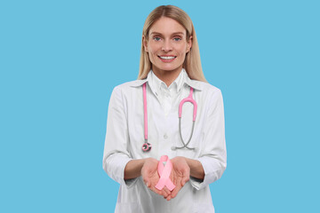Doctor with stethoscope holding pink ribbon on light blue background. Breast cancer awareness
