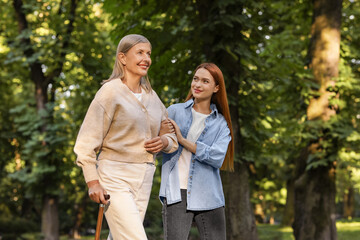 Fototapeta premium Senior lady with walking cane and young woman in park. Space for text