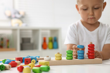 Motor skills development. Little boy playing with stacking and counting game at table indoors, closeup