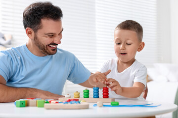 Motor skills development. Father and his son playing with stacking and counting game at table indoors