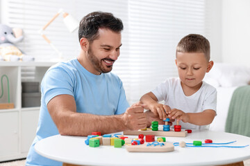 Motor skills development. Father and his son playing with stacking and counting game at table indoors