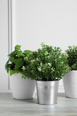 Different artificial potted herbs on wooden table near white wall, space for text