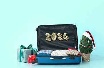 Suitcase with clothes, figure 2024 made of balloons, Christmas tree and gifts on color background