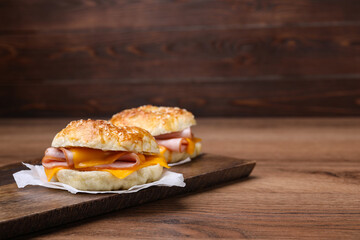 Delicious bagels with ham and cheese on wooden table. Space for text