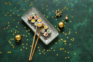 Plate with tasty sushi rolls and Christmas decor on green background - obrazy, fototapety, plakaty