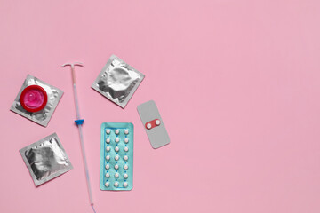 Contraception choice. Pills, condoms and intrauterine device on pink background, flat lay. Space...