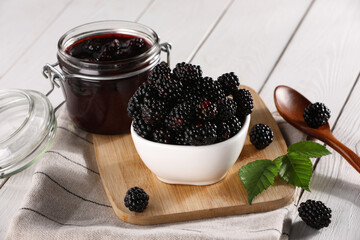 Fresh ripe blackberries, tasty jam and leaves on white wooden table