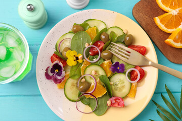 Delicious salad with orange, spinach, olives and vegetables served on turquoise wooden table, flat lay