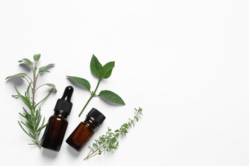 Bottles of essential oils and different herbs on white background, flat lay. Space for text