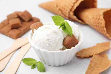 Scoops of tasty ice cream with mint leaves and caramel candies on white table, closeup