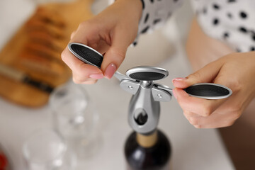 Woman opening wine bottle with corkscrew at table, above view