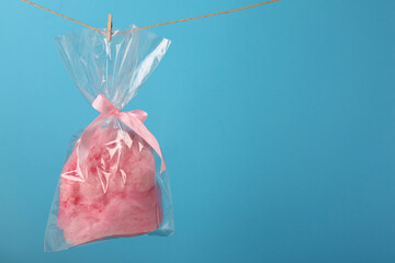 Packaged sweet pink cotton candy hanging on clothesline against light blue background, space for...
