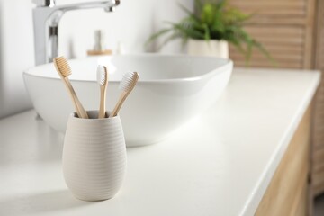 Bamboo toothbrushes on white countertop in bathroom, space for text