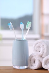 Plastic toothbrushes in holder and towels on wooden table indoors