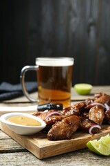 Tasty roasted chicken wings served with beer on wooden table, closeup
