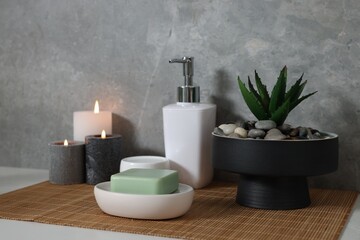 Potted artificial plant, soap, burning candles and bamboo mat on white table