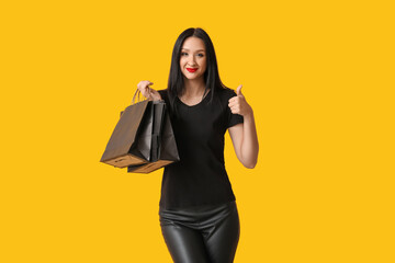 Beautiful stylish woman with shopping bags showing thumb-up gesture on yellow background. Black Friday Sale