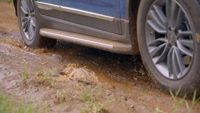 Car passing through a dirt road, navigating through a mud puddle.