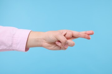 Woman crossing her fingers on light blue background, closeup