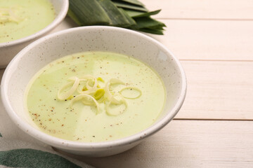 Bowl of tasty leek soup on white wooden table, closeup. Space for text