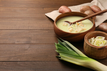 Bowl of tasty leek soup, spoon and ingredients on wooden table. Space for text