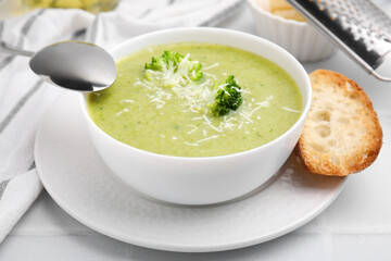 Delicious broccoli cream soup with cheese served on white tiled table, closeup