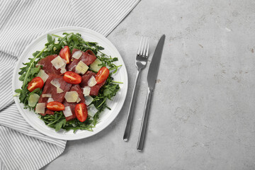 Delicious bresaola salad with parmesan cheese served on light grey textured table, flat lay. Space for text