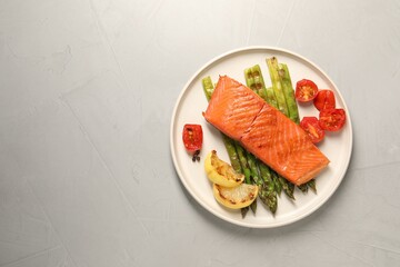 Tasty grilled salmon with asparagus, tomatoes, spices and lemon on light grey table, top view. Space for text