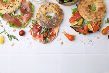 Tasty bagel sandwiches on white tiled table, flat lay. Space for text