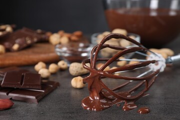 Whisk with chocolate cream and ingredients on gray table, closeup