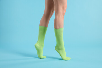 Woman in stylish lime socks on light blue background, closeup