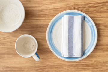 Top view of blue and white dish with folding napkin and tableware on wood background