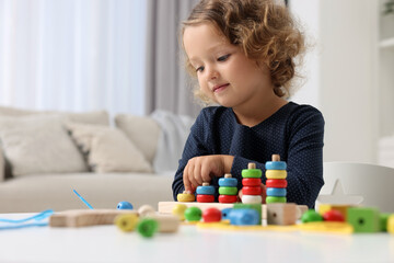 Motor skills development. Little girl playing with stacking and counting game at table indoors
