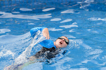 Close-up action portrait of a child swimming freestyle in an outdoor swimming pool 