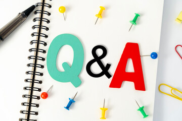 Blank multi-colored note paper with QA or questions and answers written on it. Top view of pen and glasses writing Q and A on desk.