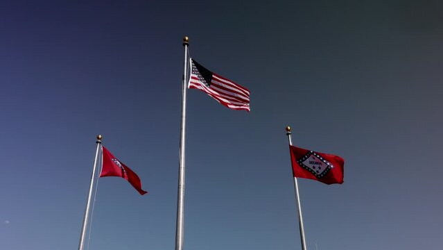 Arkansas state flags and American flag waving in the wind in slow motion.
